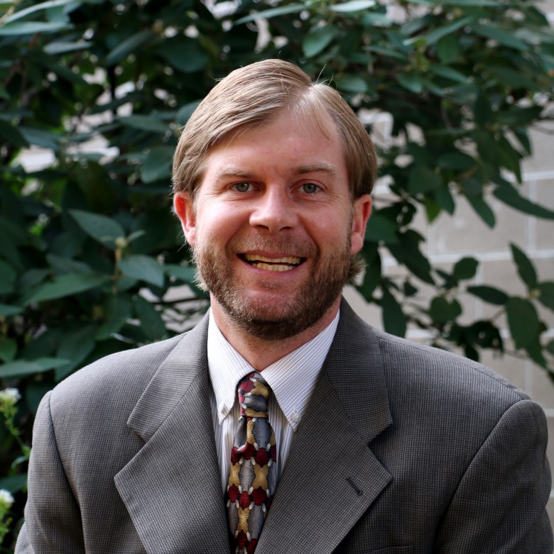 Jared Richardson, Team Leader, Oil and Gas and OPA Support, stands outside wearing business attire in front of a leafy green background.