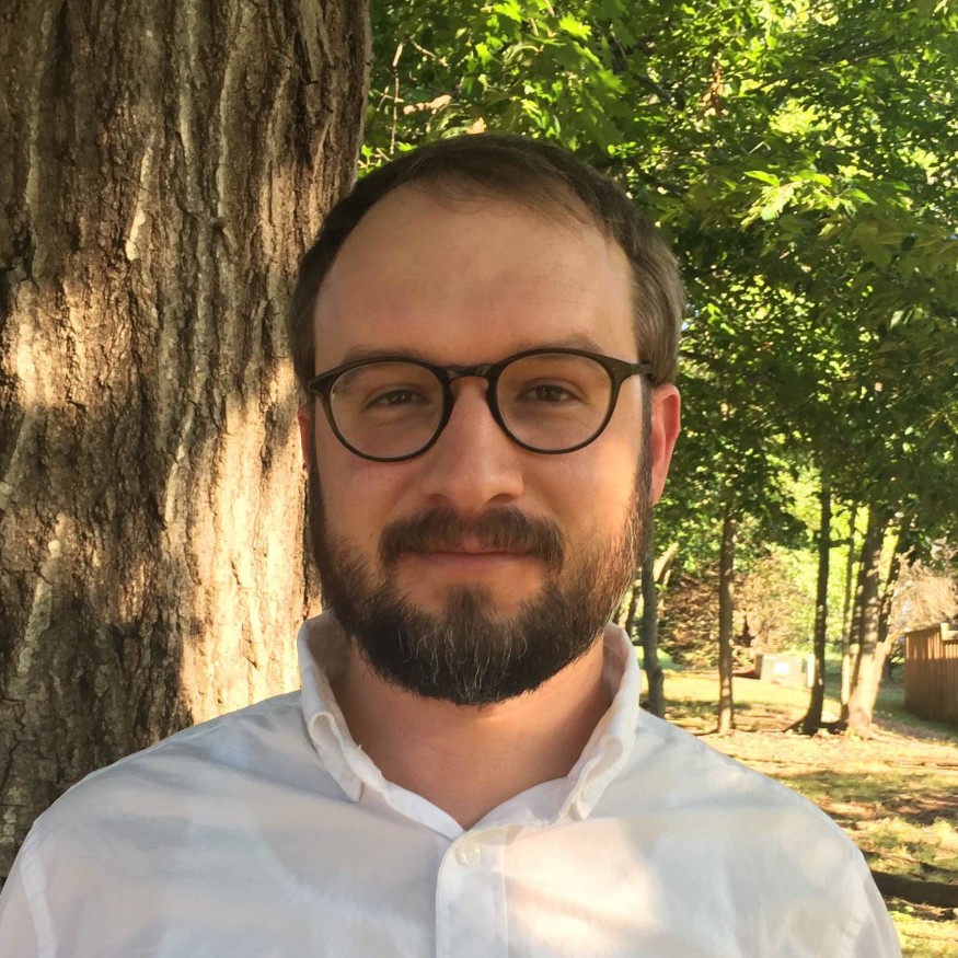 Matt Reusswig, Civil Engineer, Permitting Tools, Analysis, and Cost Estimation, stands outside wearing business casual attire by a tree with a sunny, forested background.