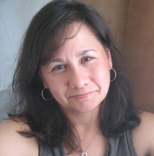 Ann Foxwell, Senior Environmental Scientist, stands wearing business casual attire in front of a light brown and grey background.