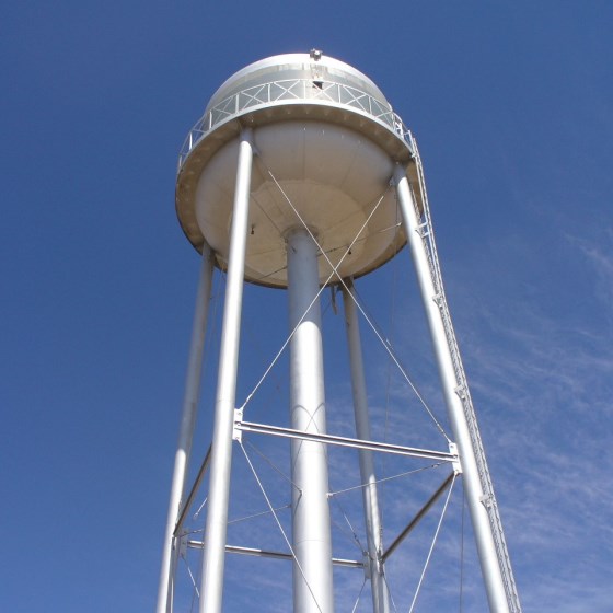 Looking up at the belly of a large grey water tower amid blue skies on a sunny, clear day.