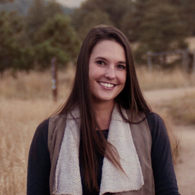 Kettie Holland Rupnik, Environmental Scientist, stands outside wearing business casual attire in front of a hiking trail with pine trees in the background.