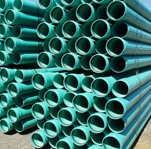 A stack of turquoise PVC water main piping still bailed together from transport. With the open ends facing towards you, the mid-day sun highlights the blue color.