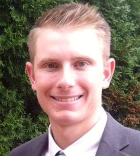 Collin Mummert, Environmental Scientist, stands outside wearing business attire in front of a leafy green background.