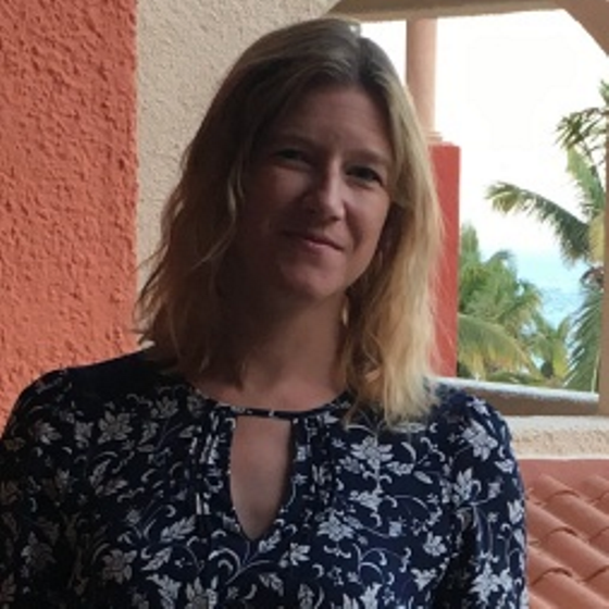 Tiffany Brackett, Senior Environmental Scientist, stands wearing business attire on a balcony in front of a red terracotta and white stucco structure. Palm trees are visible in the background to the right.