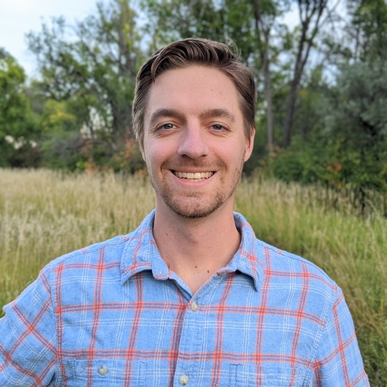 Kevin Stockton, Environmental Scientist, stands wearing business casual attire in a grassy landscape with a line of trees visible in the distance.