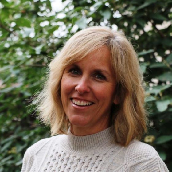 Martha Williams, Contracts Manager, stands outside wearing business attire in front of a sunlit leafy green background.