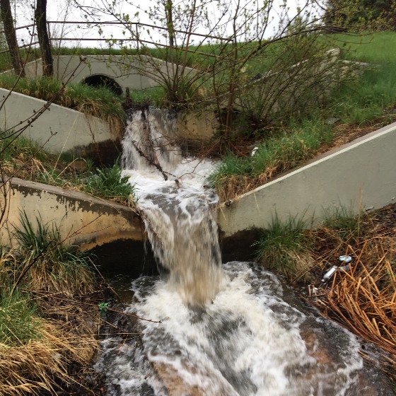 Stormwater flowing towards you down a tiered concrete channel through a grassy area.