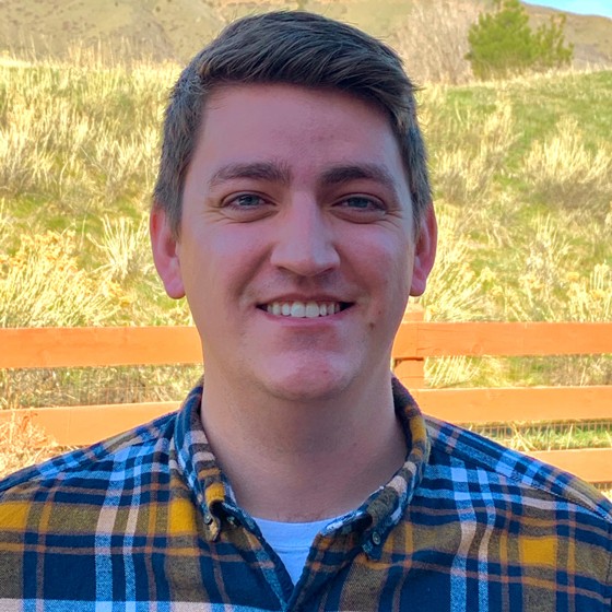 Taylor Mears, Contracts Representative, stands in business casual attire in front of a yellow and green grassy area.