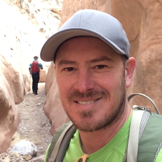 Nick Bruno, Licensed Operator, stands wearing hiking gear with a slot canyon in the background.