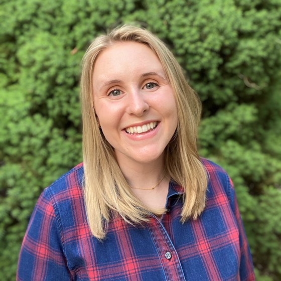 Ali Sutphin, Environmental Scientist, stands outside wearing business casual attire in front of a leafy green background.