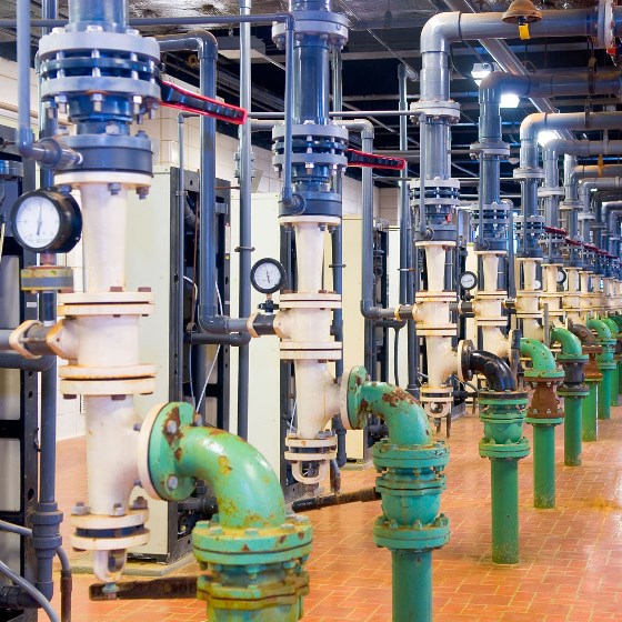 Interior of a drinking water treatment plant with a row of white, blue, and green vertical pipes and tiled floor.