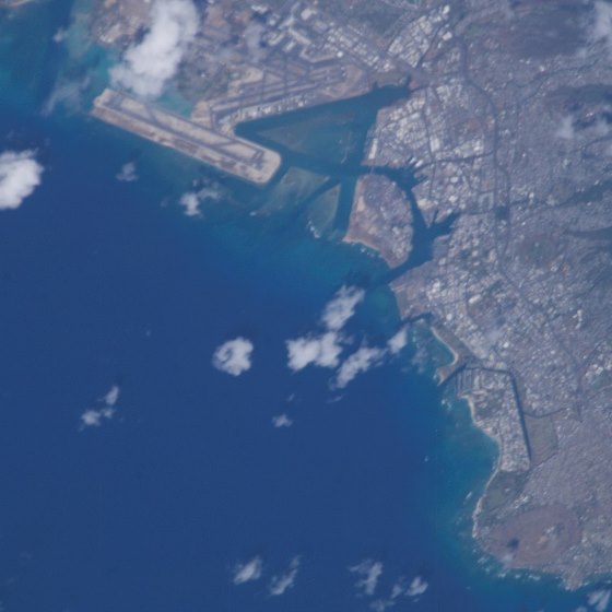 An image of Hawaii taken from space, depicting the developed coastline and the surrounding deep blue seas with just a few small white clouds over the scene.