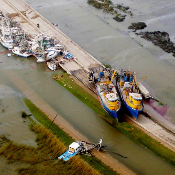 Aerial photo of several damaged boats are strewn across the landscape, surrounded by floodwaters following a severe storm.