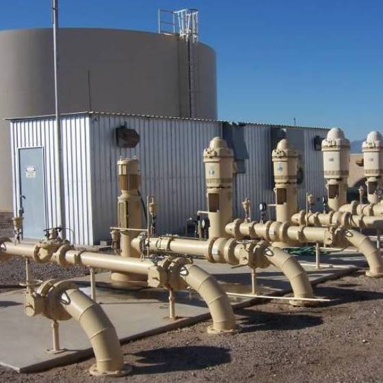 A series of beige groundwater well pumps at a water facility under a clear blue sky.