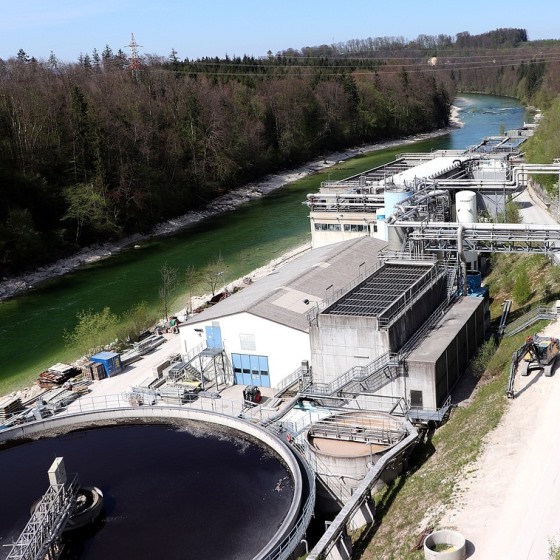 Overhead image of wastewater treatment facility adjacent to a river lined by trees.